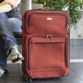 Επιβάτης με σαγιονάρα δίπλα σε βαλίτσα ετοιμάζεται για καλοκαιρινές διακοπές