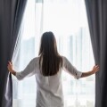 Γυναίκα ανοίγει κουρτίνες σε δωμάτιο