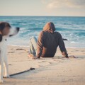 Άνδρας καθιστός στην παραλία μαζί με τον σκύλο του