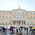 Πολίτες με ομπρέλες εν μέσω βροχής μπροστά από το μνημείο του Άγνωστου Στρατιώτη και τη Βουλή