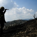 Πυροσβέστης με τη μάνικα ανά χείρας ρίχνει νερό σε καμένο τοπίο