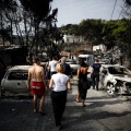 Πολίτες περπατούν ανάμεσα σε καμένα οχήματα την επομένη της τραγωδίας στο Μάτι