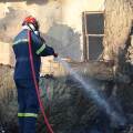Πυροσβέστης ρίχνει νερό σε φωτιά έξω από καμένο σπίτι στη Σαλαμίνα