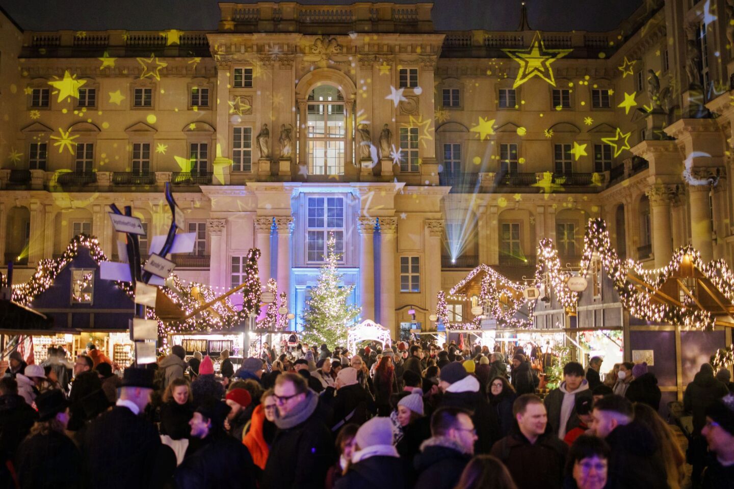 Οι επισκέπτες στέκονται μέσα στη φωτισμένη αυλή κατά τη διάρκεια της χειμερινής αγοράς στο Χούμπολτ του Βερολίνου στη Γερμανία