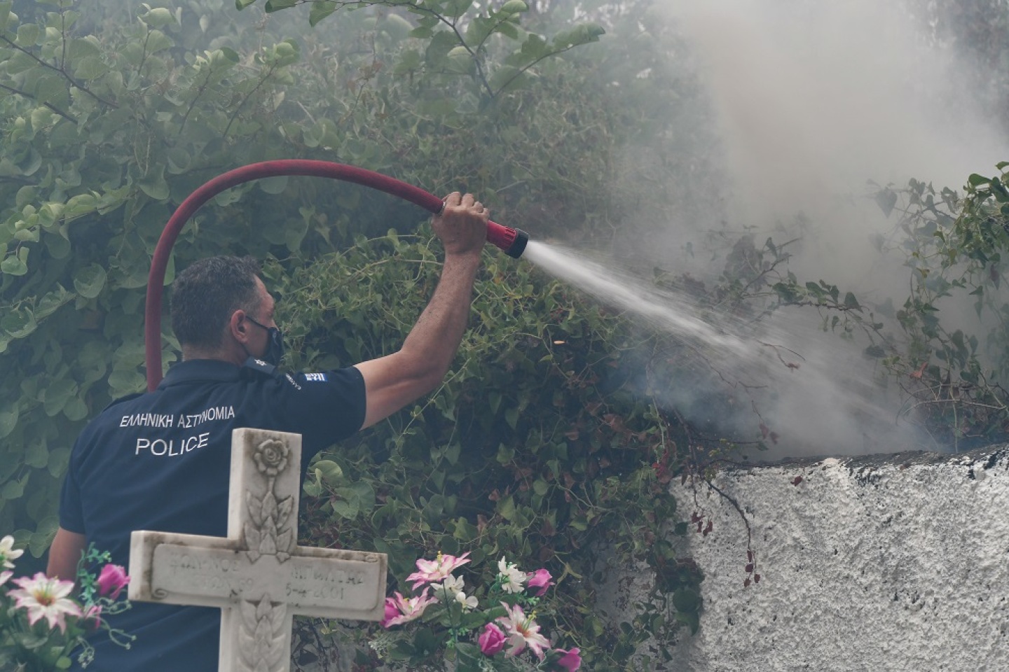 Αστυνομικός επιχειρεί να σβήσει τις φωτιές που έχουν κυκλώσει το νεκροταφείο στην περιοχή Αφίδνες, στη Βόρεια Αττική. 