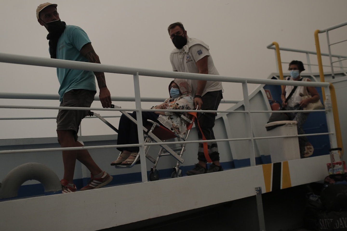 Άνδρες μεταφέρουν ηλικιωμένη κάτοικο του χωριού Πευκί, στο κατάστρωμα φέρι μποτ το οποίο βρίσκεται σε αναμονή στην παραλία του χωριού για να συνδράμει στην εκκένωση του χωριού