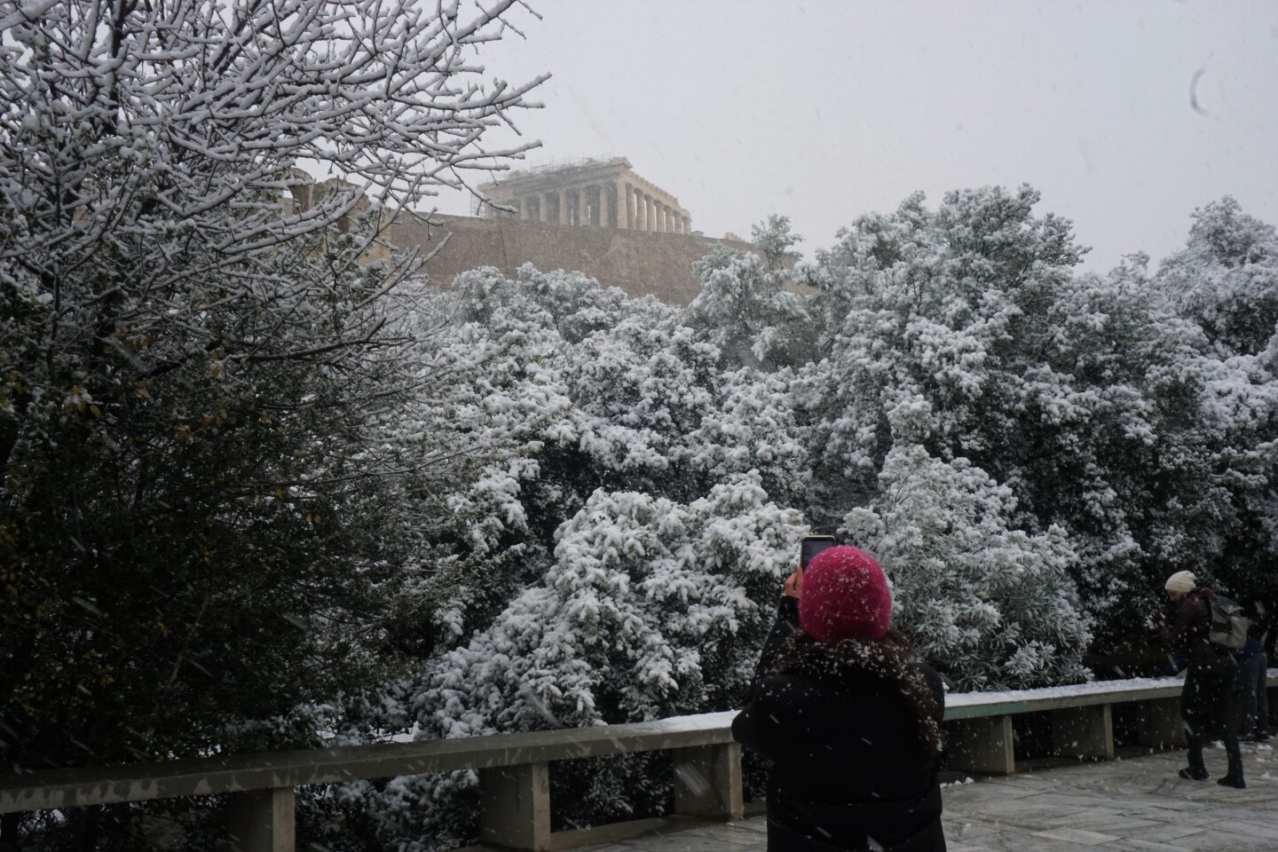 Μια γυναίκα τραβάει φωτογραφία την χιονισμένη Ακρόπολη.