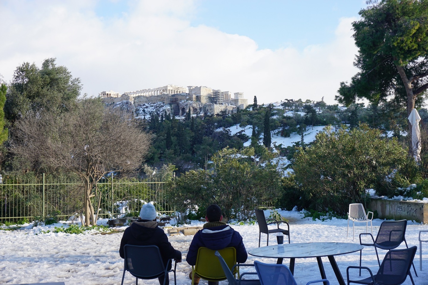 Δύο άτομα κάθονται και απολαμβάνουν την θέα της Ακρόπολης.