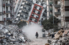 Γυναίκα στην πόλη Χατάι περπατά μπροστά από σπίτι που έχει γείρει μετά τον καταστροφικό σεισμό στην Τουρκία