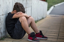 Νεαρό αγόρι κάθεται στο έδαφος σκυμμένο και κρύβει το πρόσωπό του