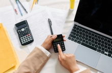 Δύο χέρια χειρίζονται calculator πάνω από ένα laptop μαζί με λογιστικά έγγραφα