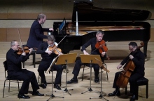 4 μουσικοί με έγχορδα, βιολί - βιολοντζέλο σε παράσταση. Από πίσω τους ένα πιανίστας παίζε με μαύρο πιάνο με ουρά