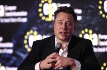 Ο Έλον Μασκ καθιστός με ένα μικρόφωνο στο χέρι σε συνέντευξη