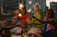 Έξι άτομα καθισμένα υψώνουν τα ποτήρια τους κρατώντας κεριά