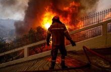 πυροσβέστης με καφέ στολή και μάσκα μπροστά από φωτιά