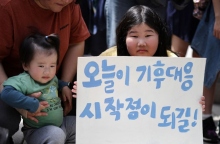 Νεαρή Κορεατισσα κρατάει πινακίδα δίπλα σε γονέα με ένα μωρό