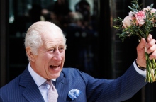 Άνδρας με ριγέ μπλε σακάκι χαμογελάει κρατώντας λουλούδια