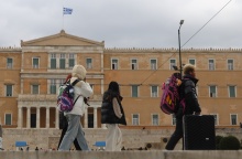 Άτομα με ζεστά ρούχα και μπουφάν περπατούν μπροστά από τη Βουλή