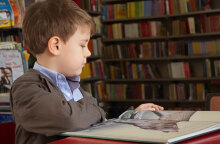 boy sitting near red table reading book