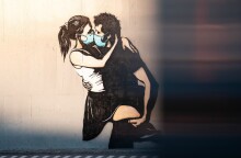 Stencil όπου απεικονίζεται αγόρι να φιλά κορίτσι με χειρουργικές μάσκες