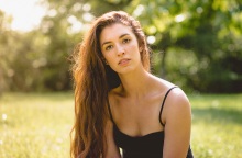 Γυναίκα με μακριά καστανά μαλλιά και μαύρη μπλούζα με τιράντα με φόντο δέντρα