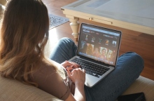 Γυναίκα κάθεται στον καναπέ με το λάπτοπ στα πόδια της