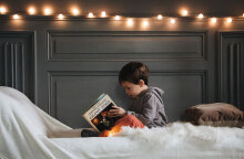 Αγοράκι καθισμένο σε κρεβάτι κρατώνας βιβλίο στα χέρια του