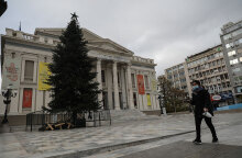 Γυναίκα με προστατευτική μάσκα περνά μπροστά από το Δημοτικό Θέατρο Πειραιά, όπου έχει στηθεί ένα τεράστιο χριστουγεννιάτικο δέντρο
