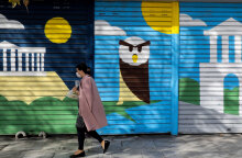 Lockdown στην Αττική για τον κορωνοϊό: Γυναίκα με μάσκα περνά μπροστά από γκράφιτι στο κέντρο της Αθήνας