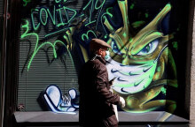 Άνδρας με μάσκα περνά μπροστά από γκράφιτι για τον κορωνοϊό