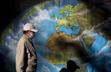 Άνδρας με προστατευτική μάσκα για τον κορωνοϊό περνά μπροστά από γκράφιτι με τον παγκόσμιο χάρτη της Γης