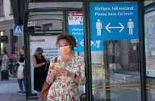 Κορωνοϊός: Κοπέλα με μάσκα και το κινητό στο χέρι περιμένει σε στάση λεωφορείου