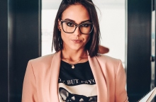 Γυναίκα στο ασανσέρ με καρέ μαλί, γυαλιά μυωπίας, μαύρη μπλούζα και ροζ σακάκι