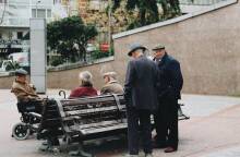 Ηλικιωμένοι άντρες στέκονται και συζητούν γύρω από ένα παγκάκι