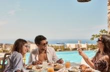 Ένας άντρας και δύο γυναίκες τρώνε πρωινό με φόντο το Αιγαίο