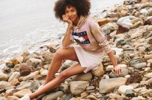 Γυναίκα με φούστ ακαι φούτερ καθισμένη σε βότσαλα δίπλα σε θάλασσα