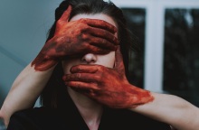 Χέρια με αίματα καλύπτουν πρόσωπο γυναίκας
