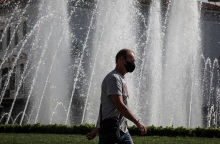Πολίτης φορά μάσκα προστασίας κατά του κορωνοϊού και περπατά μπροστά από σιντριβάνι