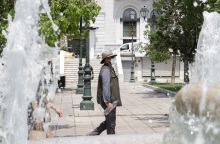 Πολίτης φορά τη μάσκα του και το καπέλο του περπατώντας στην πλατεία Συντάγματος