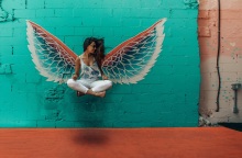 Γυναίκα που αιωρείται σε στάση οκλαδόν με φόντο γκράφιτι που δείχνει φτερά