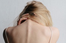 Γυναίκα με γυρισμένη πλάτη και σκυμμένο κεφάλι, κρατάει τον αυχένα της