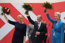 Ο Όλαφ Σολτς και το επιτελείο του υψώνουν το χέρι τους κρατώντας ανθοδέσμες