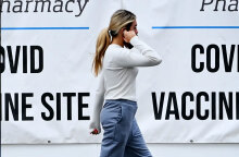 Κοπέλα στις ΗΠΑ μιλά στο κινητό, περνώντας μπροστά από αφίσες για τον εμβολιασμό κατά του κορωνοϊού