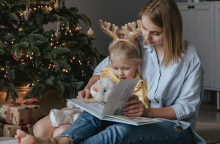 Μαμά και παιδί διαβάζουν βιβλίο δίπλα από το χριστουγεννιάτικο δέντρο