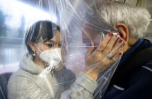 Γυναίκα με μάσκα στην Ιταλία αγκαλιάζει ηλικιωμένο σε γηροκομείο, έχοντας ανάμεσά τους μια ειδική πλαστική κουρτίνα