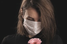 Γυναικά με μάσκα κρατά στα χέρια της ένα λουλούδι