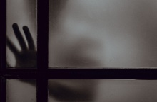 Χέρι και πρόσωπο διακρίνεται πίσω από κλειστή πόρτα σε ημίφως