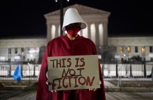 Άνθρωπος ντυμένος με κόκκινο μανδύα και καπέλο που κρατά πινακίδα υπέρ των αμβλώσεων