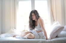 Γυναίκα καθισμένη σε κρεβάτι κρατάει την κοιλιά της με δυσφορία