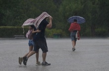 Πολίτες προστατεύονται από τη βροχή με πανωφόρι ή ομπρέλα